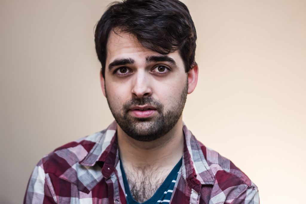 Early 30s white man with dark brown shaggy hair, a close-cropped beard, a plaid shirt, and an obscene amount of chest hair showing